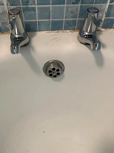 A new pair of chrome pillar taps on a white bath against blue mosaic tiles, the left one with a red disc on top and the right one with a blue disc