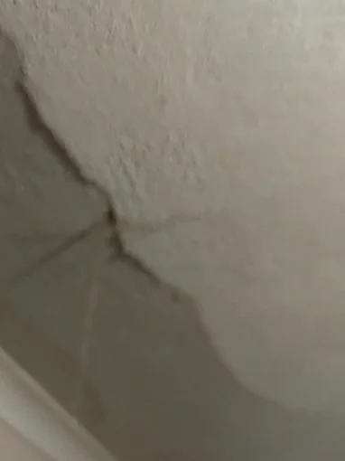 A ceiling with a long crack running across it and a darker band of water stained plaster spreading out along the crack