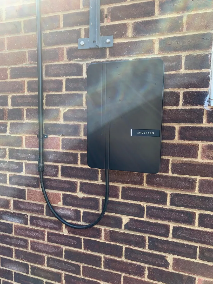 A black Andersen EV charge point mounted flush on a dark brick wall with the charging cable concealed and looped below the unit