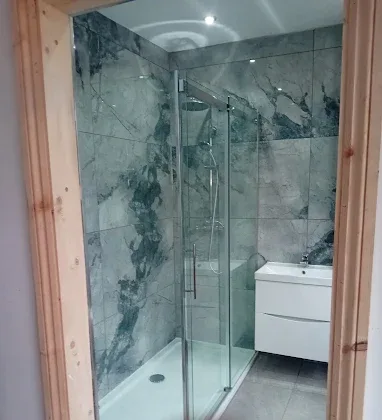 Finished shower room with marble effect tiles, a glass sliding enclosure and a white wall hung vanity