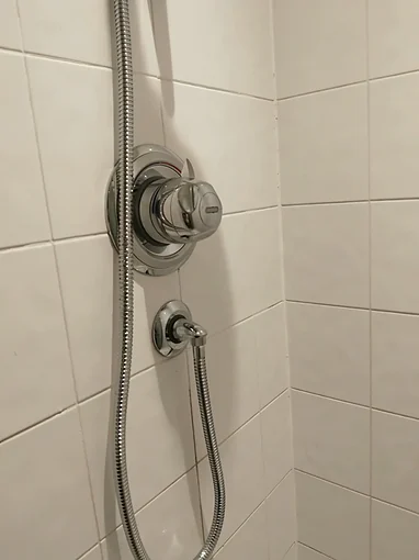 A new chrome concealed shower valve with a round plate and a lever on the dial, set on white wall tiles, with a separate round wall outlet below it and a chrome hose on its elbow