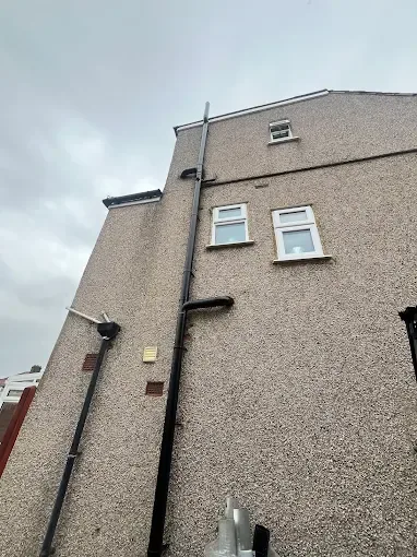 New black soil stack running the full height of a three storey gable wall on a pebbledash London property