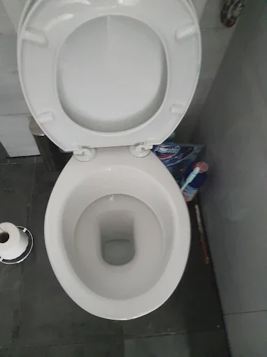 A newly fitted white close coupled toilet with the seat raised, in a grey tiled bathroom