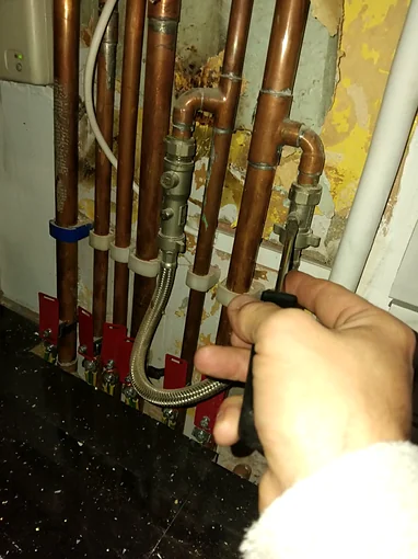 The valve on a braided filling loop being opened, in among the copper pipework under a boiler