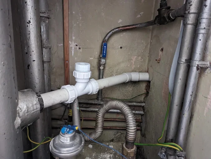 A service cupboard with lagged risers on both sides, a new white waste run with an access cap fitted across the back wall, an isolating valve on the copper feed, and a meter low in the frame